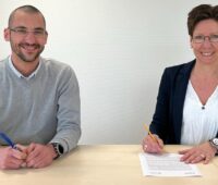 Ein Mann und eine Frau an einem Tisch, sie unterschreibt den Lizenz-Vertrag für die OPV-Technologie.