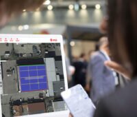 Zwei Personen betrachten einen Bildschirm mit K2 Base. Die Software zeigt ein Luftbild eines Gebäudedachs mit eingezeichneten PV-Modulfeldern.