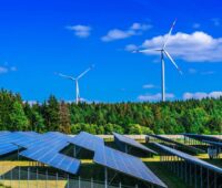 Ein Solarpark neben einem Wald und Windenergieanlagen.