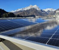 Photovoltaik-Dachanlage vor der Silhouette schneebedeckter Berge.