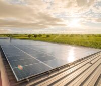 PV-Anlage im Vordergrund, Windpark im Hintergrund vor untergehender Sonne.