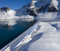 Zu sehen ist die geplante Photovoltaik-Anlage an der Muttsee-Staumauer als Visualisierung an der realen Staumauer in der schneebedeckten Berglandschaft.