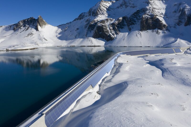 Zu sehen ist die geplante Photovoltaik-Anlage an der Muttsee-Staumauer als Visualisierung an der realen Staumauer in der schneebedeckten Berglandschaft.