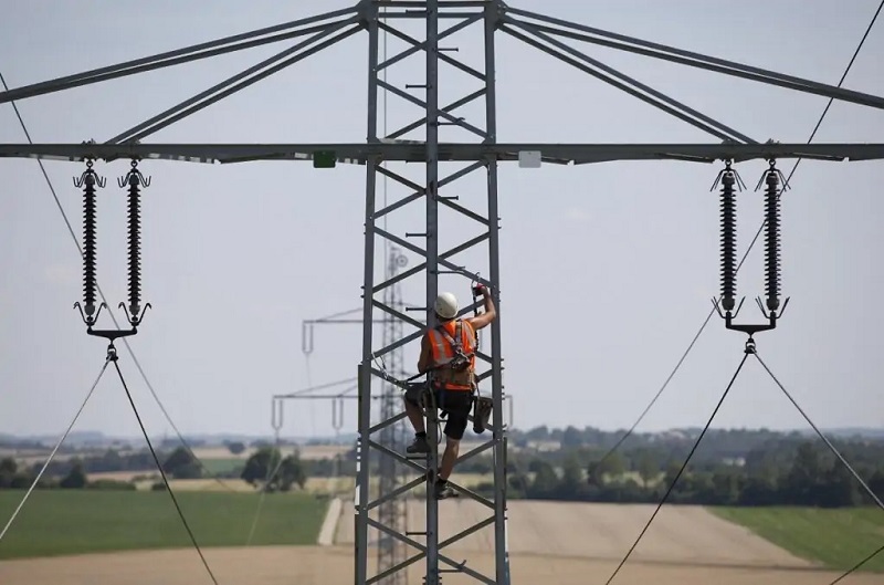 Zu sehen ist ein Arbeiter, der auf einen Strommast einer Hochspannungsleitung klettert. Die Bundesnetzagentur setzt die Eigenkapitalkosten für Strom- und Gasnetzbetreiber fest.