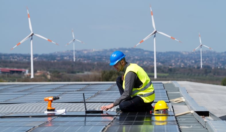 Zu sehen ist die Montage einer Photovoltaik-Dachanlage, im Hintergrund sind Windenergieanlagen. Die BMWi-Langfristszenarien unterschätzen laut BEE die nationalen Potenziale für erneuerbare Energien.