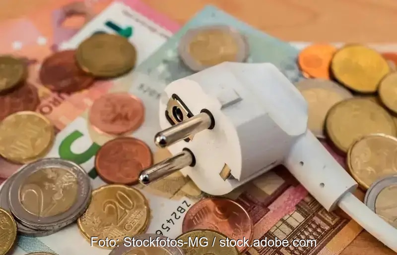 Ein Schuko-Stecker liegt auf einigen Geldscheinen und Münzen, Symbol für Strompreis.