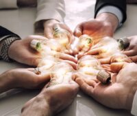 Viele Hände halten leuchtende Glühbirnen als Symbol für die EnWG-Novelle zum Energy Sharing.