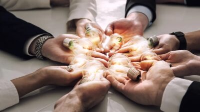 Viele Hände halten leuchtende Glühbirnen als Symbol für die EnWG-Novelle zum Energy Sharing.