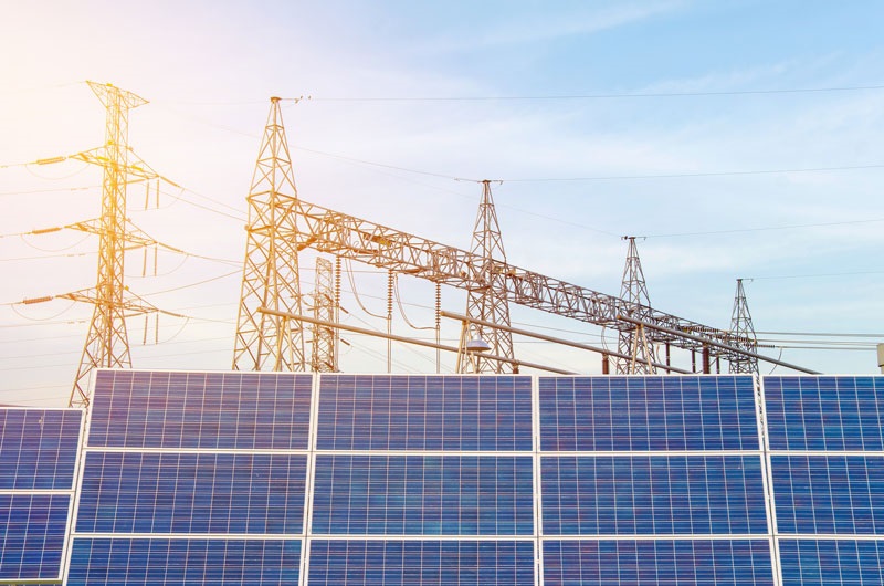 Zu sehen ist eine PV-Anlage vor Strommasten. In der Verbändeanhörung der EEG-Novelle geht es um die zukünftigen Bedingungen beim PV-Zubau.