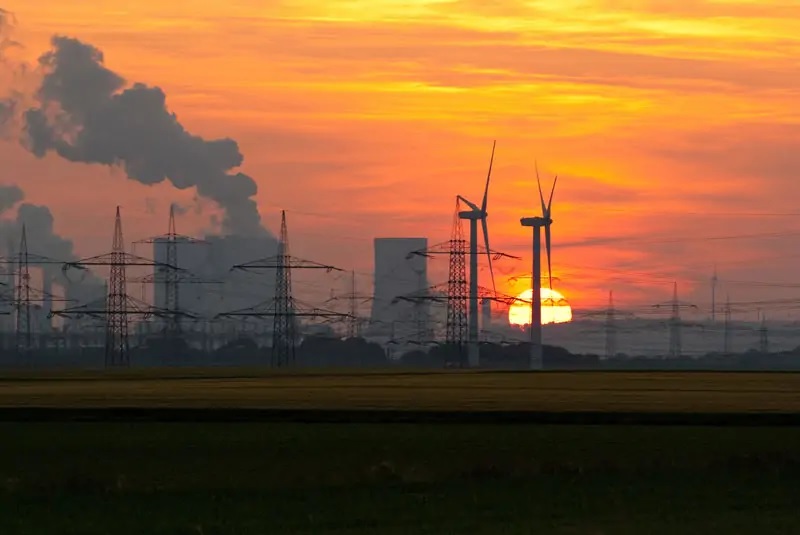 Zu sehen ist ein Kohlekraftwerk im romantischen Abendhimmel mit zwei verlorenen Windkraftanlagen im Vordergrund als Symbol für die handwerklichen Mängel im EEG 2021