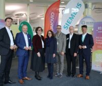 Sieben Personen in einem mit Unternehmensflaggen und Infotafeln ausgerüstetem Innenraum.