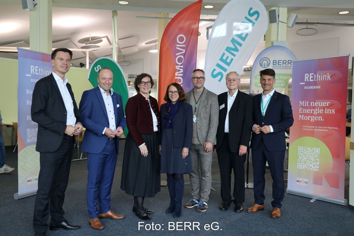 Sieben Personen in einem mit Unternehmensflaggen und Infotafeln ausgerüstetem Innenraum.