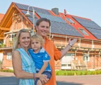 Zu sehen ist eine Familie vor ihrem Neubau, der mit der BEG-KfW-Neubauförderung gefördert werden könnte.