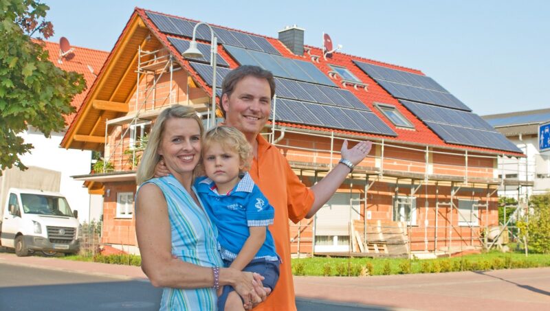 Zu sehen ist eine Familie vor ihrem Neubau, der mit der BEG-KfW-Neubauförderung gefördert werden könnte.