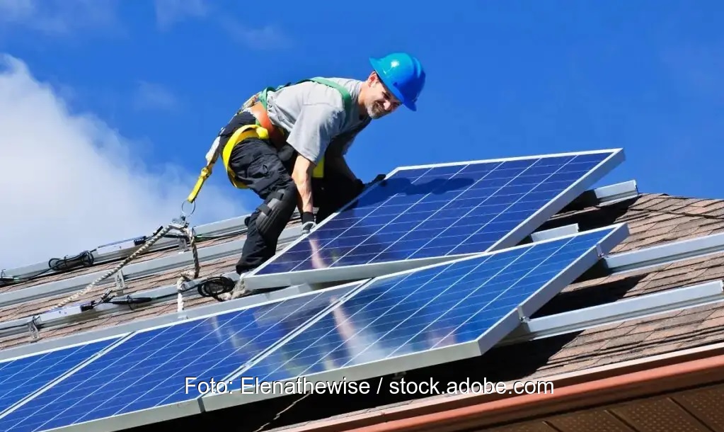 Photovoltaik-Installation: Ein Arbeiter montiert ein Solarmodul auf einem Schrägdach - Symbolbild.