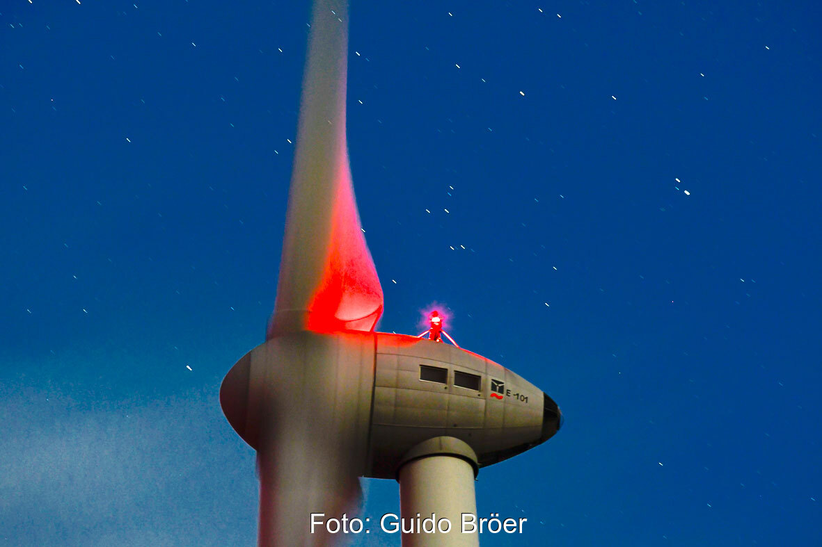 Nachtaufnahme (Langzeitbelichtung) der Gondel einer Enercon-Windenergieanlage Typ E-101 Mit roter Nachtbeleuchtung vor Sternenhimmel.