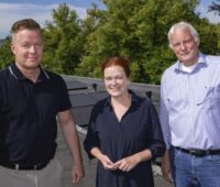 Eine Frau und zwei Männer auf einem Dach mit PV-Modulen.