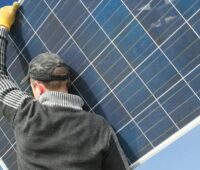 Im Bild trägt ein Mann ein Solarmodul für eine Installation einer Photovoltaik Anlage in Deutschland.