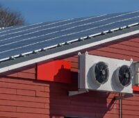 Eine Klimaanlage an einer Hauswand mit Photovoltaik auf dem Dach.