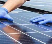 Im Bild zwei Hände mit blauen Handschuhen auf PV-Modulen als Symbol für die Forderung vom BSW-Solar zum Solarpaket I.