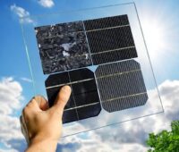Eine Hand hält eine transparente Platte mit vier unterschiedlich strukturierten Solarzellen gegen einen blauen Himmel mit Wolken.
