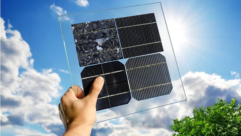 Eine Hand hält eine transparente Platte mit vier unterschiedlich strukturierten Solarzellen gegen einen blauen Himmel mit Wolken.