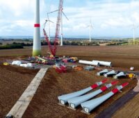 Zu sehen ist der Bau einer Windenergieanlage auf einem Acker. Windenergieanlagen in Industrie- und Gewerbegebieten sind schwierig umzusetzen.