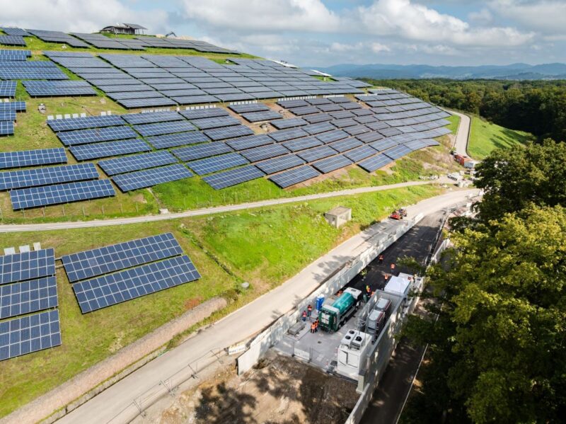 Deponieberg mit PV-Modulen und Tankstelle am Fuß des Hügels.