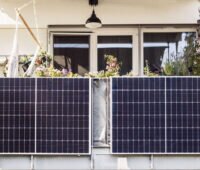 An einem Balkon eines Mehrfamilienhauses sind zwei Solarmodule nebeneinander am Balkongeländer befestigt.
