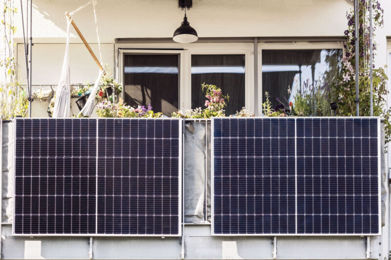 An einem Balkon eines Mehrfamilienhauses sind zwei Solarmodule nebeneinander am Balkongeländer befestigt.