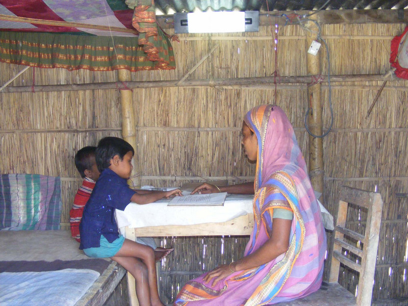 Einer Mutter mit ihren Kindern am Tisch, beleuchtet durch elektrisches Licht.