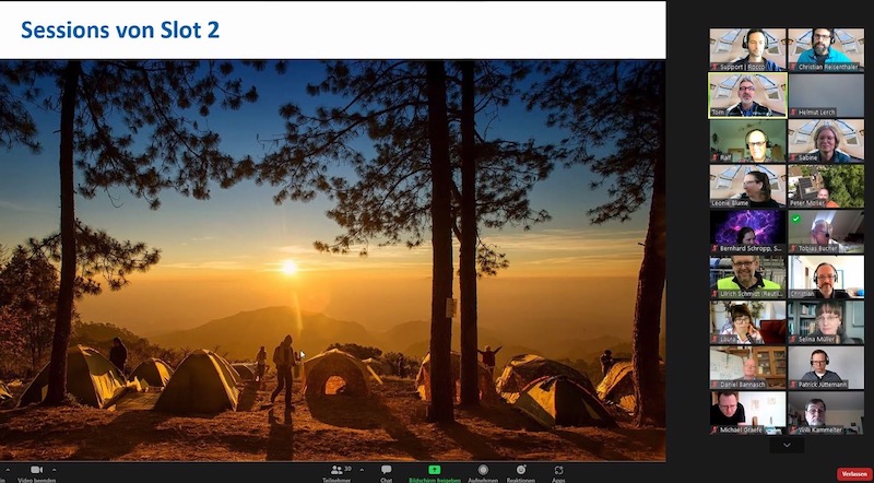 Screenshot vom Online Barcamp Renewables: Blick über eine Wiese mit Zelten und Bäumen bei Sonnenaufgang, daneben die Teilnehmenden der Online-Konferenz.