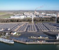 Die Visualisierung zeigt einen Batteriepark aus der Luft von schräg vorn. Im Vordergrund ein Fluss mit Schiff und Industrieanlage.