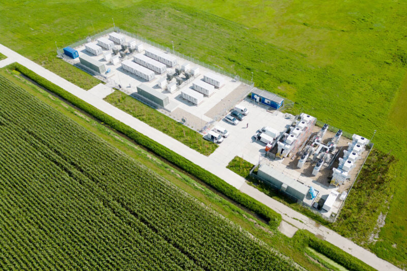 Luftbild zeigt einen großen Batteriespeicher mit mehreren Containern an einem Weg inmitten von Wiesen. Symbolbild für Flächenpooling.