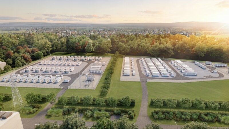 Batteriespeicerhprojekt auf der grünen Wiese mit Bäumen im Hintergrund vor dem Horizont. Aufgenommen aus der Vogelperspektive.