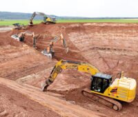 Baugrube für den Erdbecken-Wärmespeicher in Bracht. Vier große Bagger, ein Bulldozer, roter Sandstein