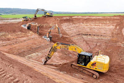 Baugrube für den Erdbecken-Wärmespeicher in Bracht. Vier große Bagger, ein Bulldozer, roter Sandstein