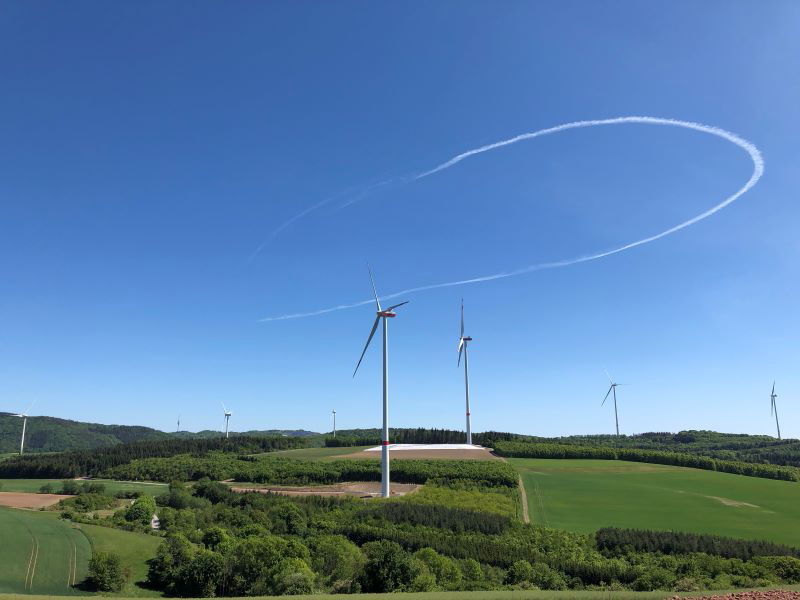 Windkraftanlagen auf welligem Terrain unter blauem Himmel.