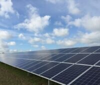 Freiflächensolaranlage auf grüner Wiese unter blauem Himmel mit Wolken.