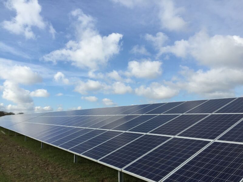 Freiflächensolaranlage auf grüner Wiese unter blauem Himmel mit Wolken.