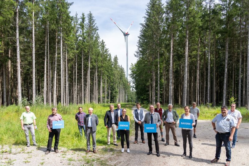 Zu sehen ist eine Menschengruppe mit Wirtschaftsminister Hubert Aiwanger im Wald vor einer Windenergieanlage bei der Auszeichnung „Gestalter der Energiewende“.