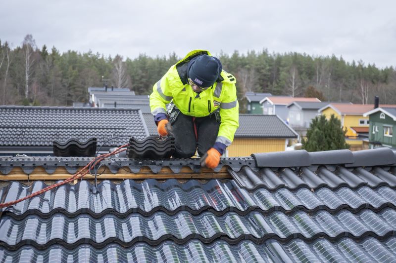 Ein Monteur installiert auf einem Dach Solarziegel, denen man die Solartechnik nicht ansieht.