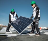 Zwei Arbeiter auf einem Hochhaus-Flachdach mit Photovoltaikmodulen.