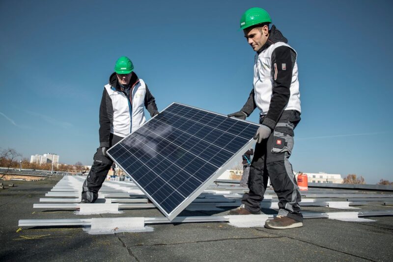 Zwei Arbeiter auf einem Hochhaus-Flachdach mit Photovoltaikmodulen.