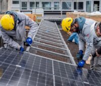 Monteure installieren PV-Module auf Gestellen auf einem Flachdach.