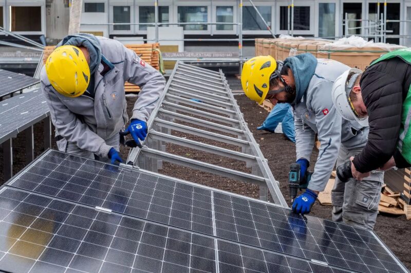 Monteure installieren PV-Module auf Gestellen auf einem Flachdach.