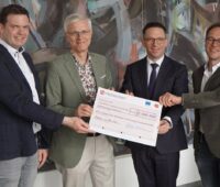 Vier Personen halten erfreut einen überdimensionierten Check über sechgs Millionen Euro in die Kamera.