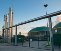 Biogas-Anlage mit zwei Kuppeln im Hintergrund, im Vordergrund Leitungen.