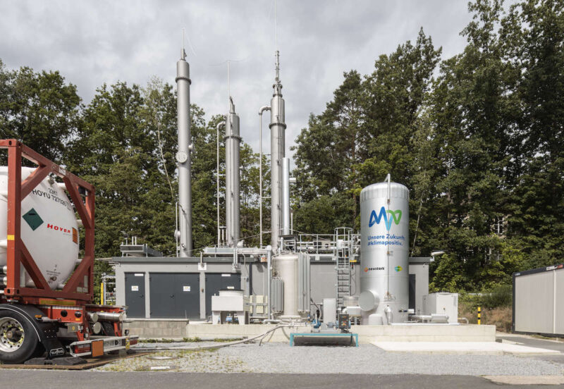 Bild zeigt Anlage von außen mit Schornstein und Tank sowie einem Lkw im Vordergrund, der das CO2 abholt.