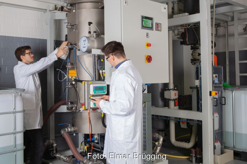 Zwei Männer in weißen Kitteln an einer Biogas-Anlage mit Hochlastfermenter.